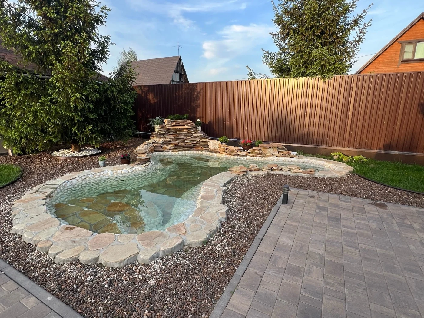 Landscaped backyard with a custom stone-edged pond, paver patio, and privacy fence
