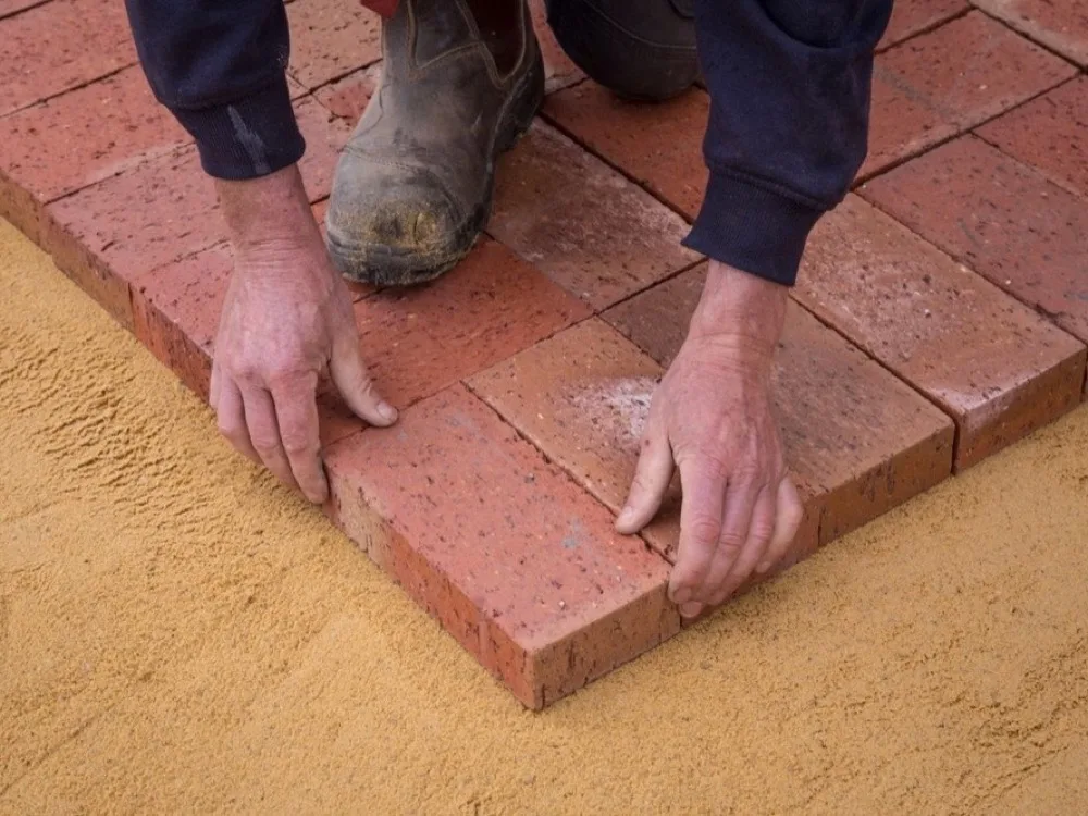 Close-up of interlocking pavers being laid on a sand base